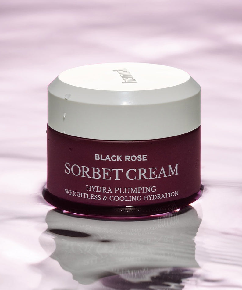 Crème HEIMISH Black Rose Hydra Plumping Shavet 50ml pour hydratation et fermeté de la peau sur fond rose liquide.