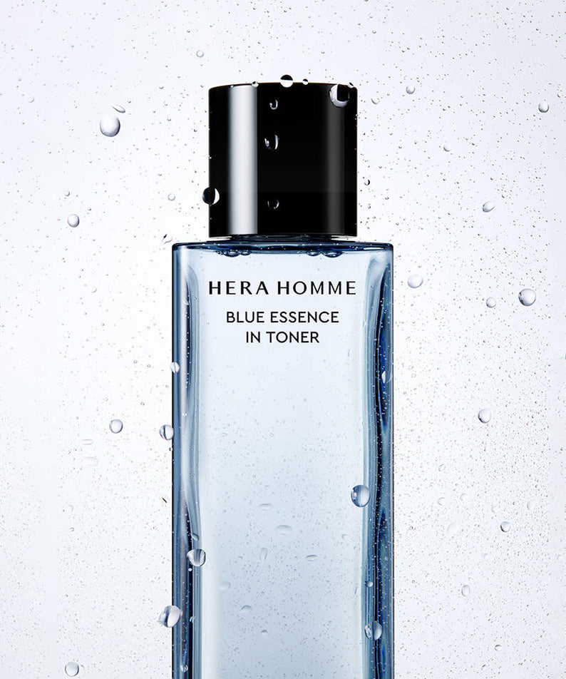 HERA  Homme Blue Essence In Toner 125ml : flacon noir/bleu sur fond clair avec gouttes d’eau, design salle de bain.