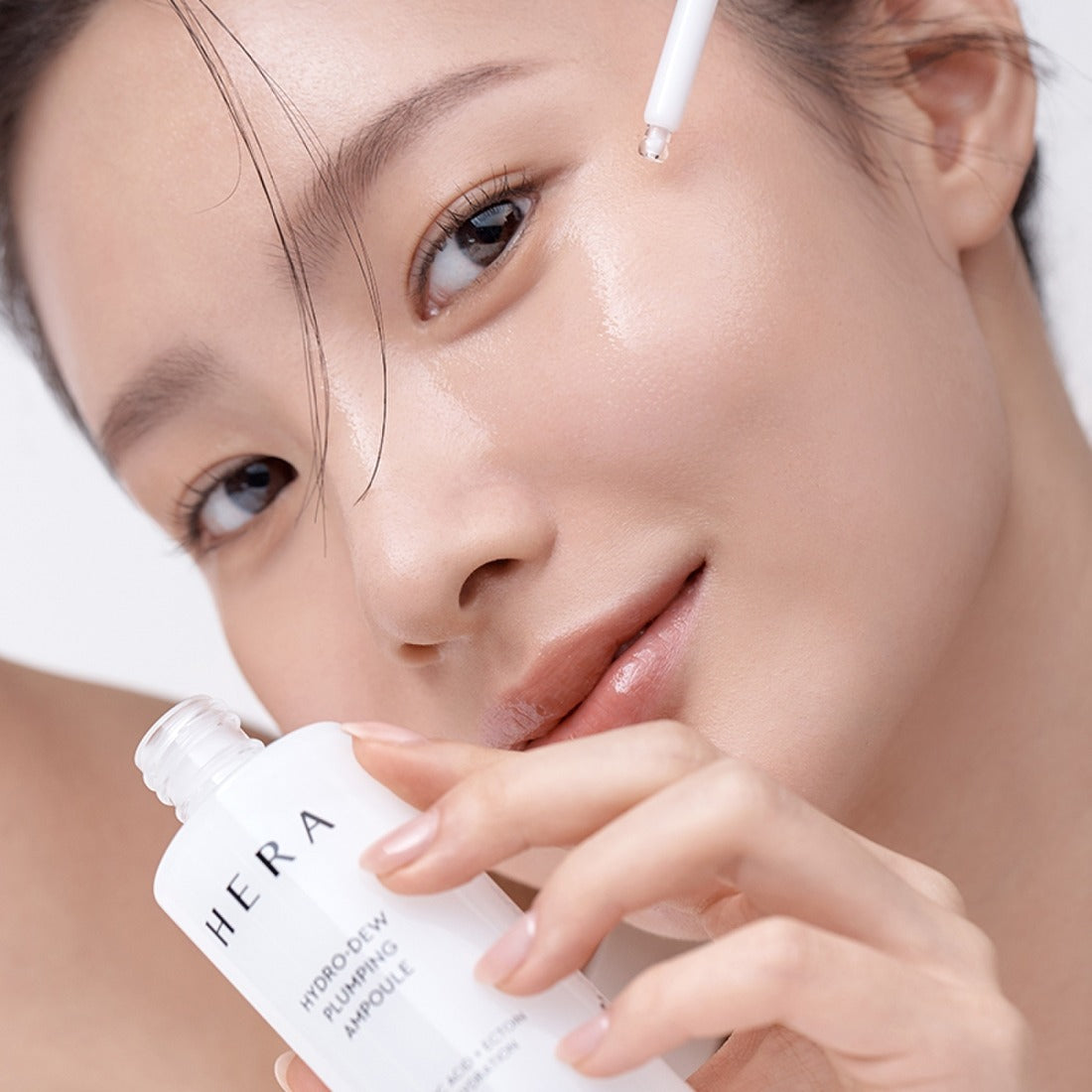 HERA Hydro-Dew Plumping Ampoule 50ml : jeune femme applique le sérum hydratant HERA sur le visage, gouttelette visible