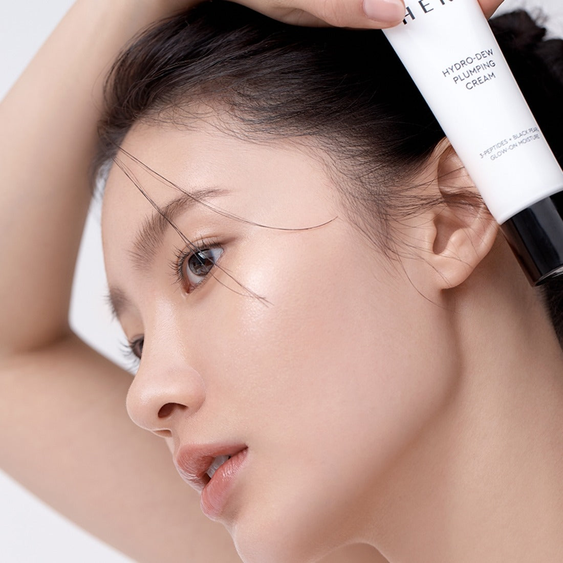 HERA Hydro-Dew Plumping Cream 50ml, gros plan sur un visage, tube de crème HERA sur la main, contexte skincare en studio