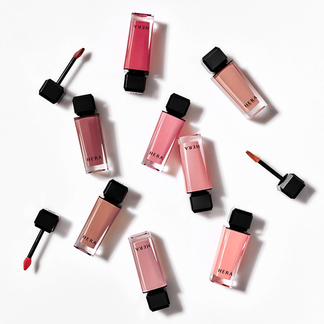 Décris l'image en français: HERA  Sensual Nude Gloss 5g, gloss nude HERA sur fond blanc, vue produit et applicateurs.