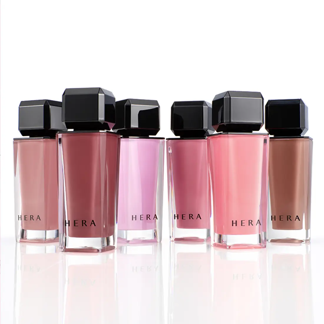HERA  Sensual Nude Gloss 5g : flacons HERA roses et nude sur fond clair, rendu maquillage brillant en studio.