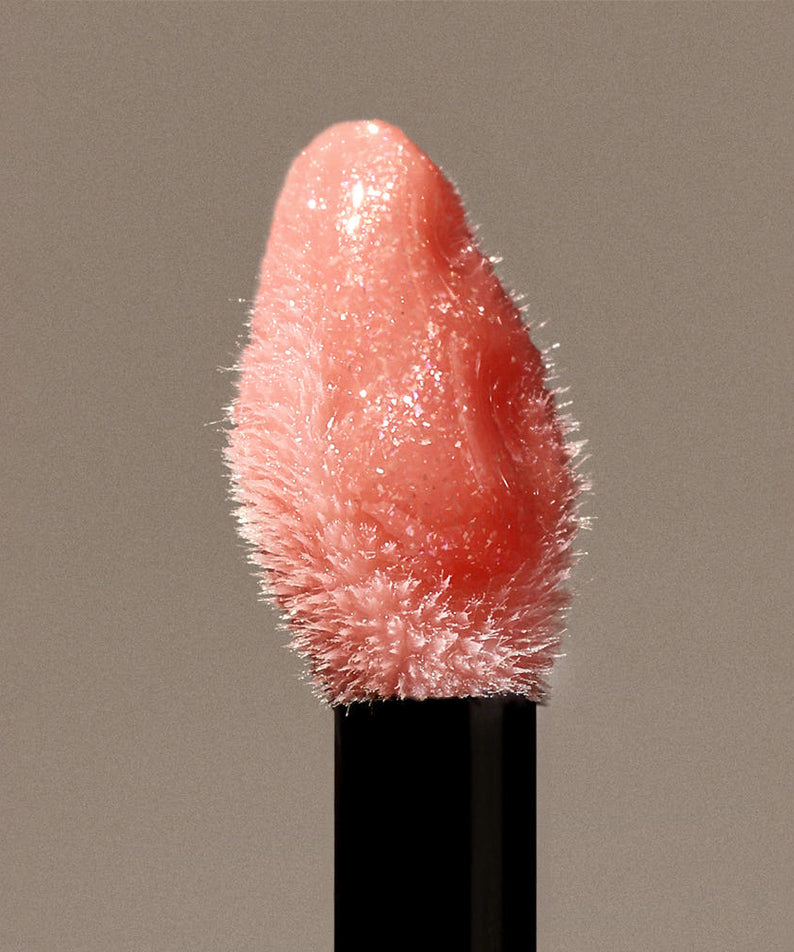 HERA  Sensual Nude Gloss 5g, rouge à lèvres brillant nude, gros plan sur le tube noir sur fond beige, éclairage doux.
