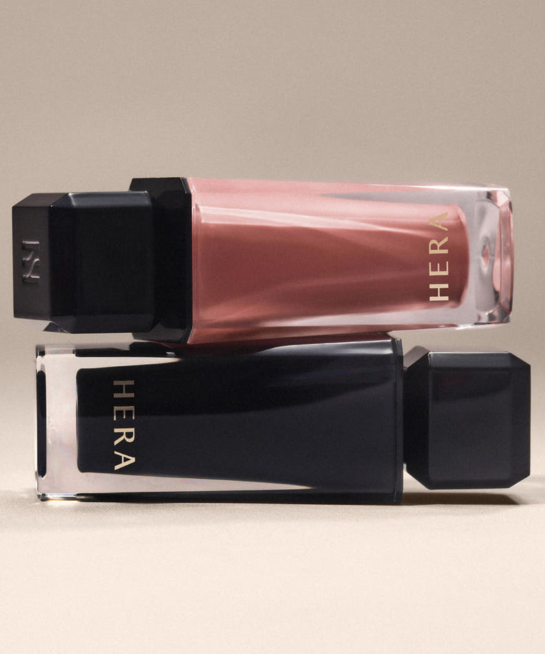 HERA  Sensual Nude Gloss 5g, marque HERA, gloss nude en tube transparent sur fond beige, prise de vue produit.