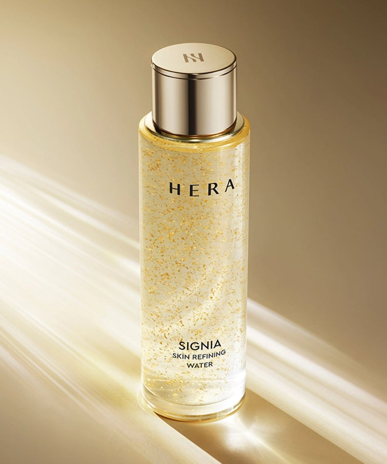HERA Signa Skin refreshing Water 180ml HERA, flacon doré sur fond beige, éclats et texture d’eau rafraîchissante