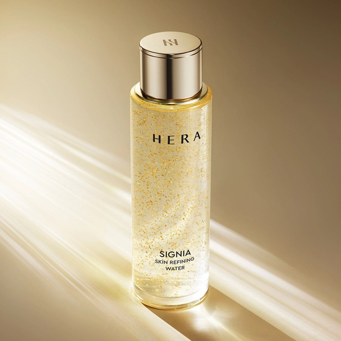 HERA Signa Skin refreshing Water 180ml HERA, flacon doré sur fond beige, éclats et texture d’eau rafraîchissante