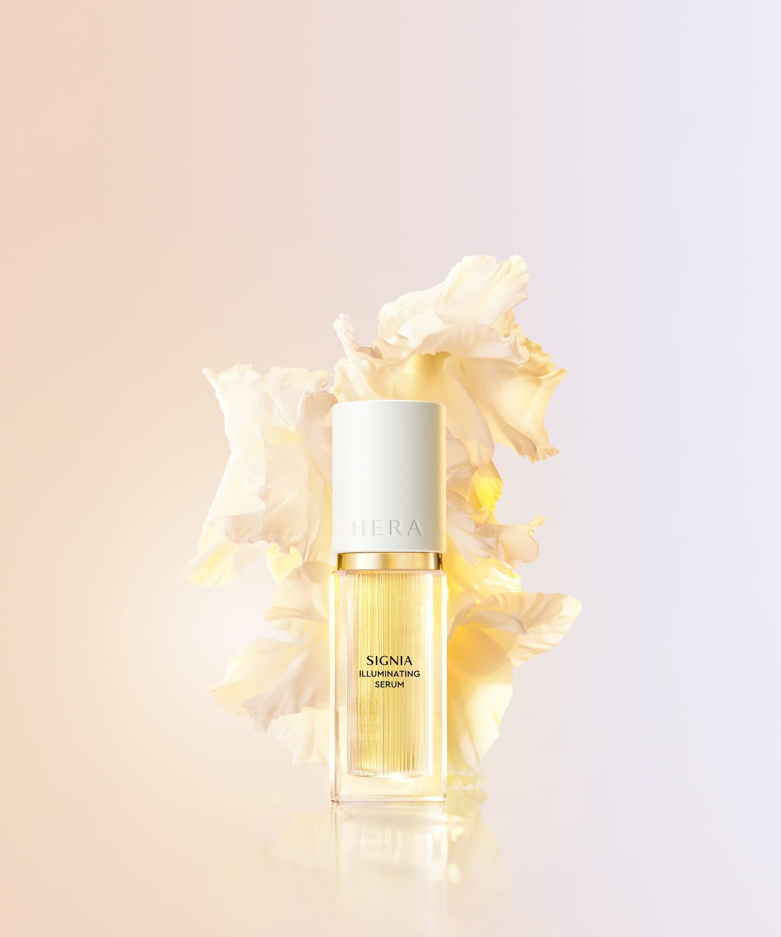 Décris l'image en français : HERA Signia Illuminating Serum 30ml, flacon doré, sur fond clair, fleurs crème en arrière-plan.