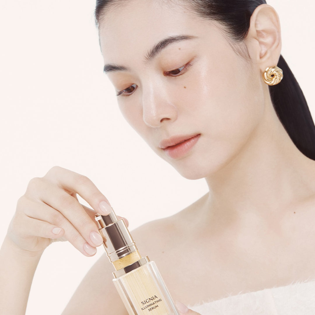 Décris l'image en français : HERA Signia Illuminating Serum 30ml de la marque HERA, sur une femme appliquant le sérum, fond clair.