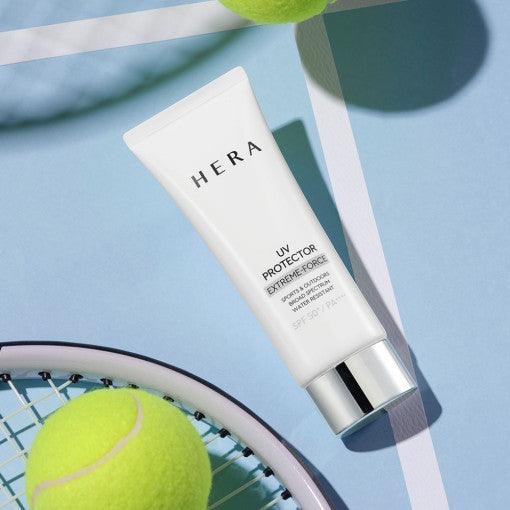 HERA UV Protector Extreme-Force Leports SPF50+PA++++, tube HERA sur fond bleu avec accessoires de tennis et balle.