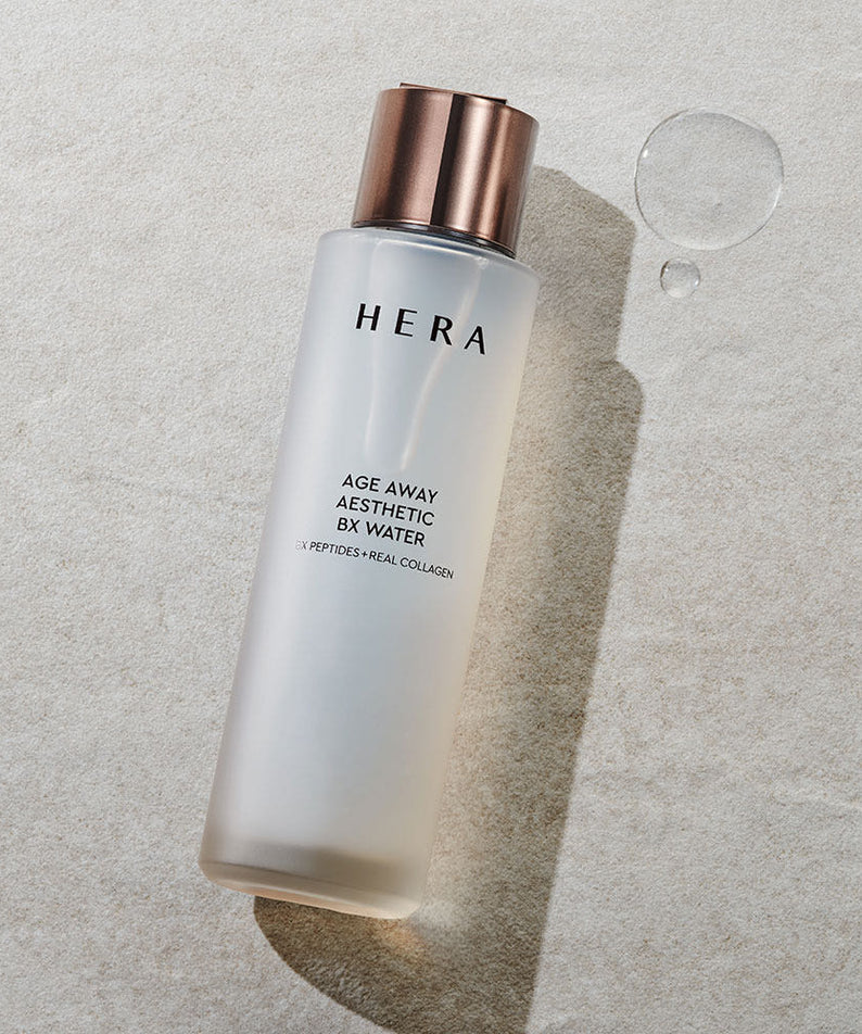HERA Age Away Aesthetic BX Water 150ml sur une surface claire avec éclaboussures.