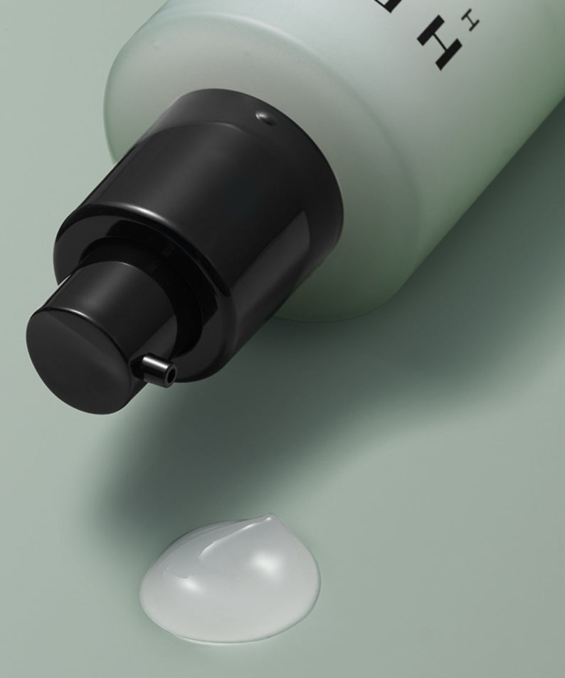 Flacon ouvert de HERA Homme All-in-One Skin Hydro Treatment 150ml avec une goutte de solution sur fond vert.