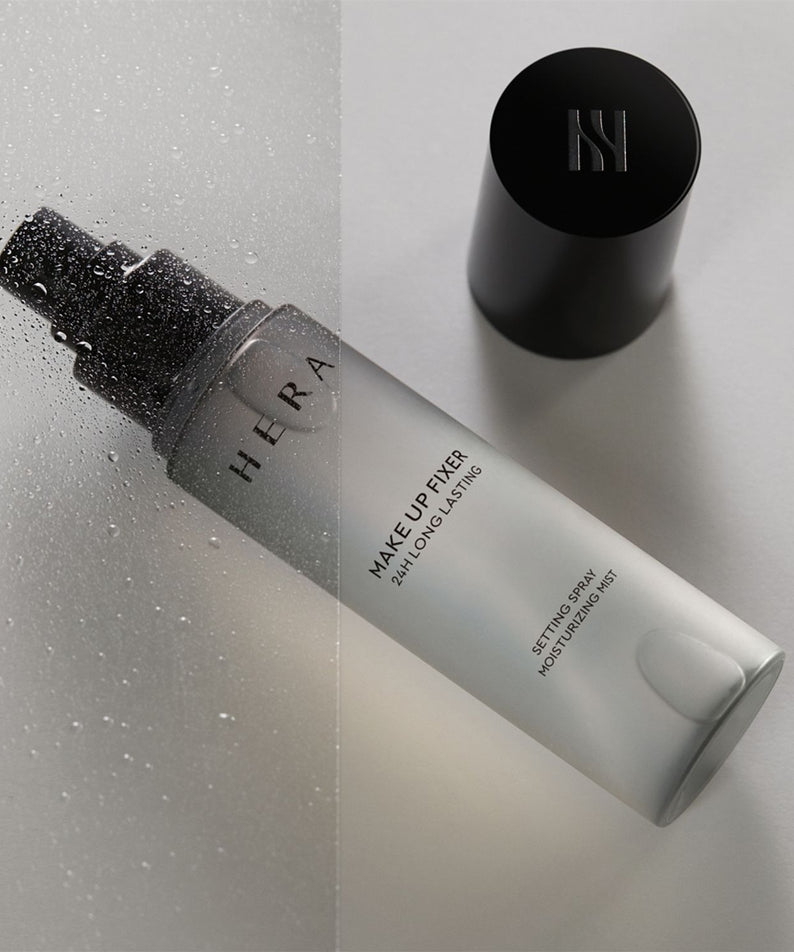 HERA Make Up Fixer 80ml vaporisateur, brume fixatrice de maquillage, photo de face sur fond de gouttelettes, couvercle noir à côté