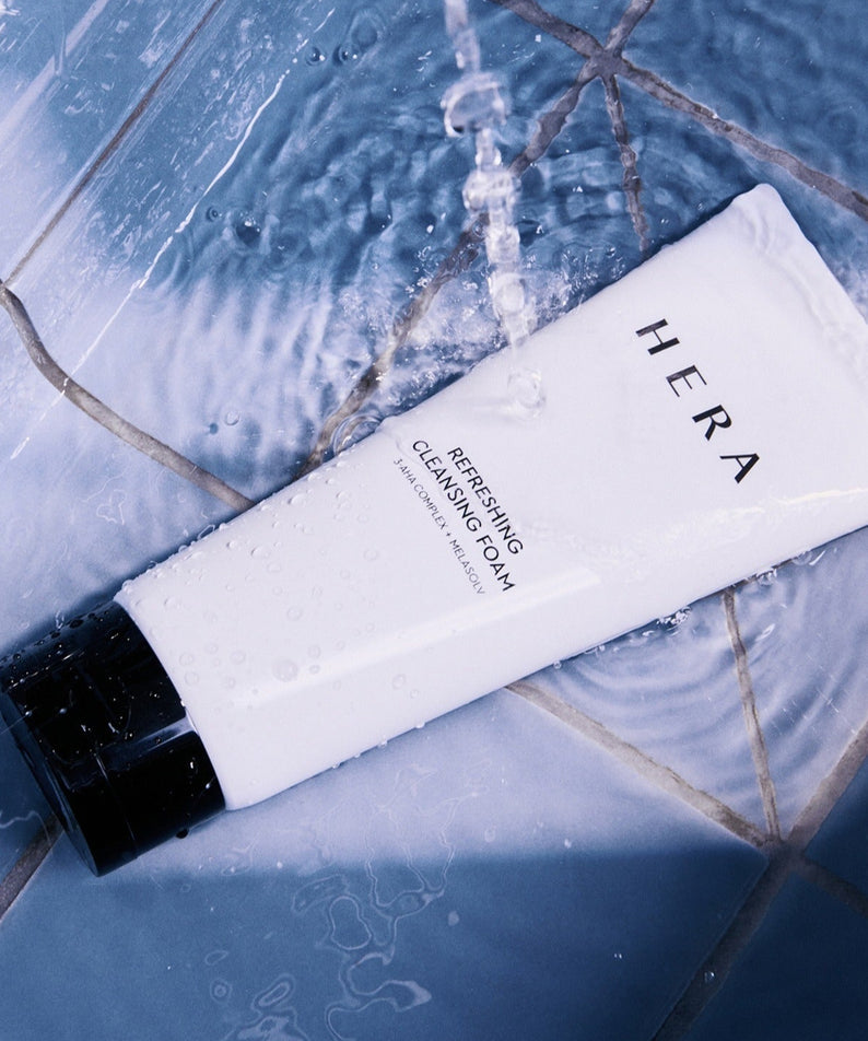 HERA Refreshing Cleansing Foam 160g sur fond de carrelage bleu mouillé, produit de soin visage, nettoyage revitalisant, beauté éclatante.