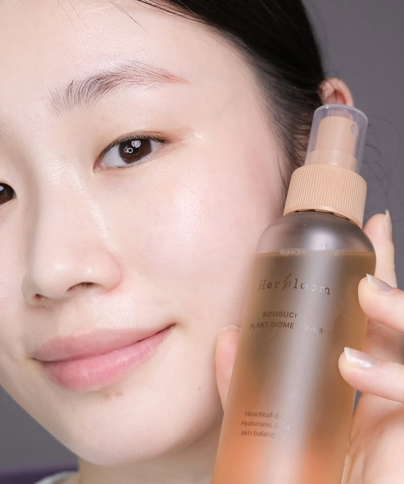 Décris l'image en français : HERBLOOM  Kombucha Plant Biome Toner 150g, femme tenant le flacon, visuel skincare en gros plan.