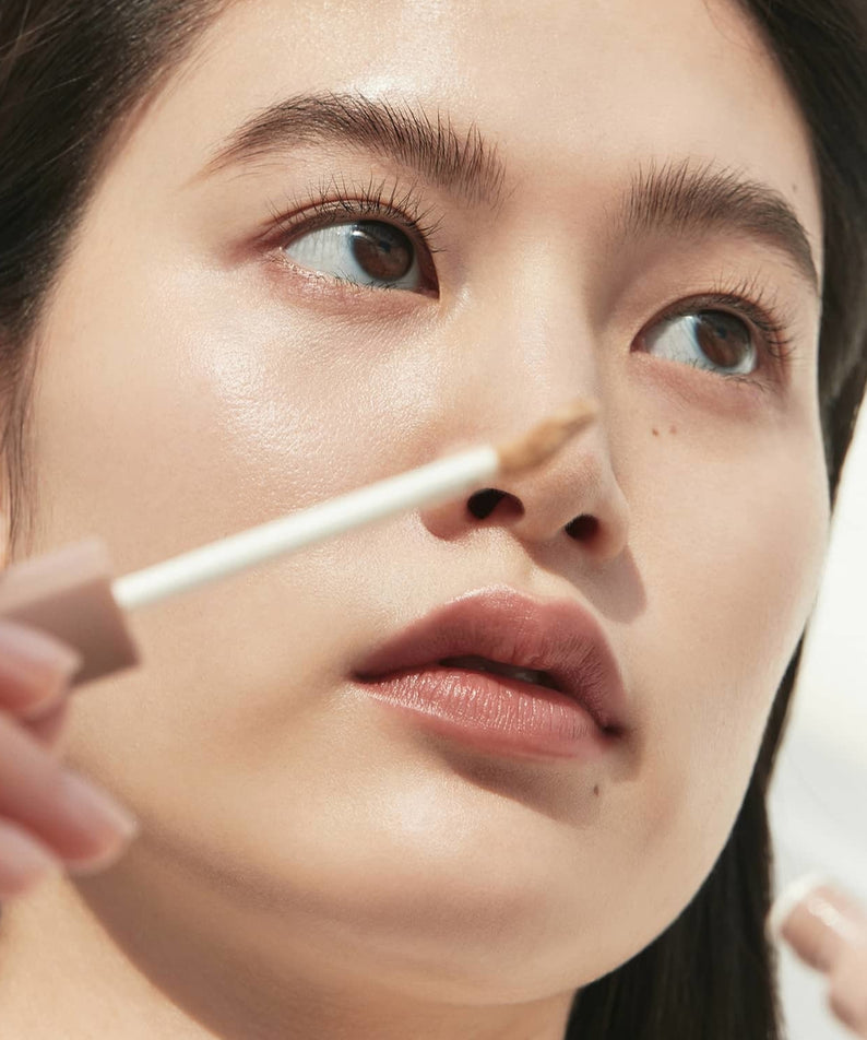 Application du HINCE Second Skin Cover Concealer pour un teint parfait et naturel, gros plan visage femme avec applicateur.