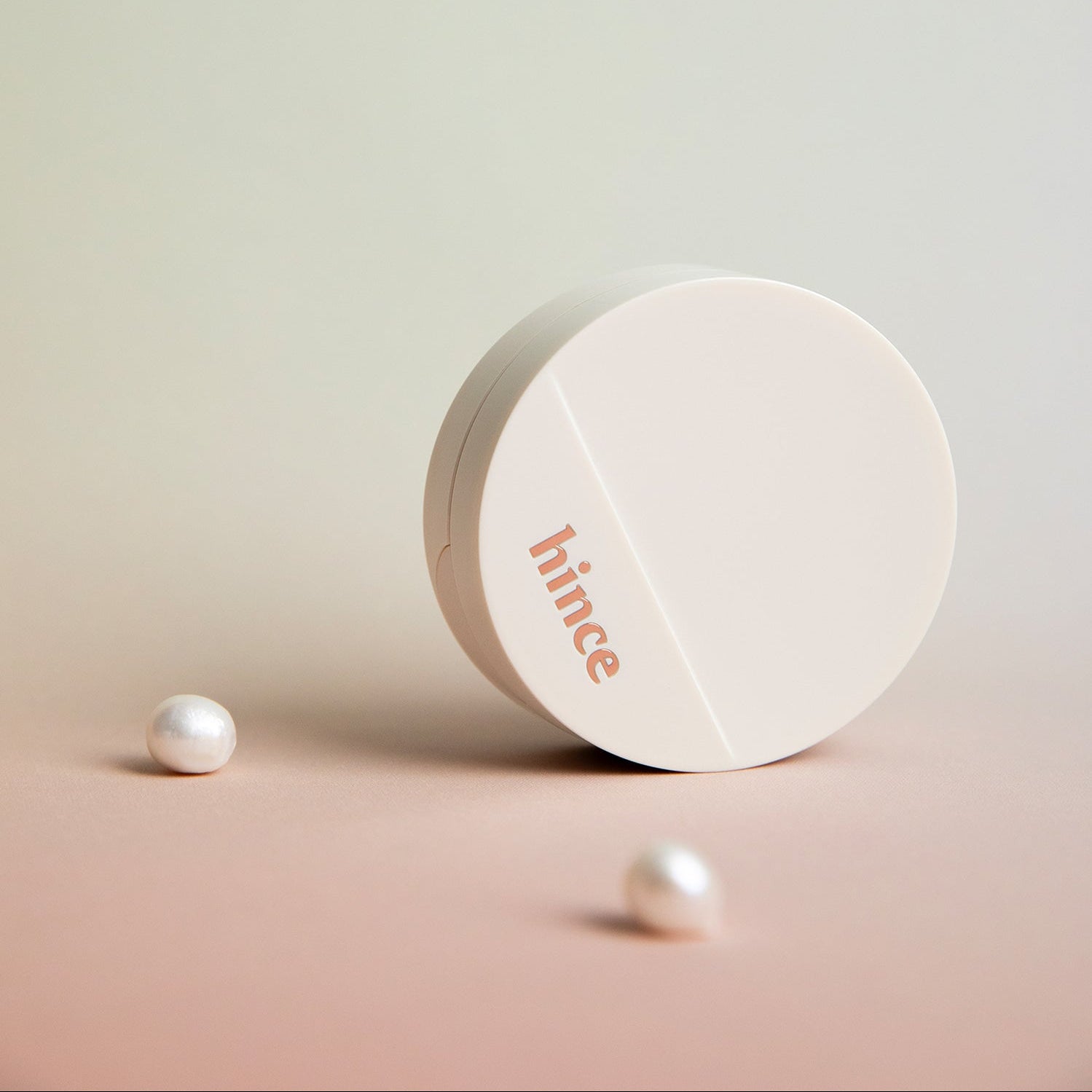 HINCE  Second Skin Glow Cushion de HINCE, boîtier blanc sur fond nude avec perles effet premium, maquillage lumineux