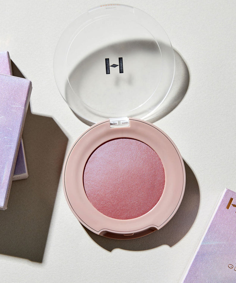 HINCE True Dimension Glow Cheek en rose pâle, avec boîtier transparent, posé sur une surface lumineuse.