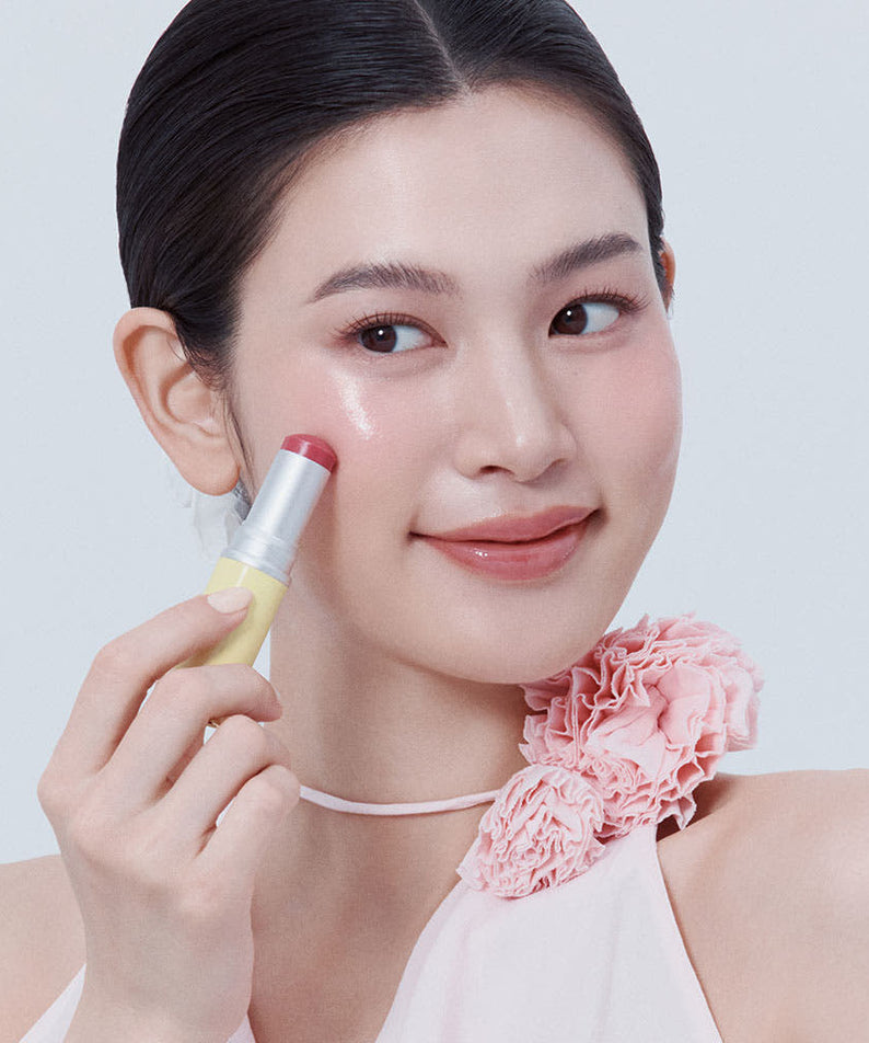 HINCE True Dimension Radiance Balm 10g : femme applique le baume sur fond clair, flacon HINCE visible, fleurs roses en décor.