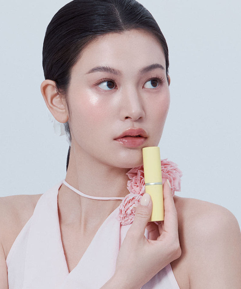 HINCE True Dimension Radiance Balm 10g de HINCE, femme maquillée tenant le baume, fond clair, rose pâle