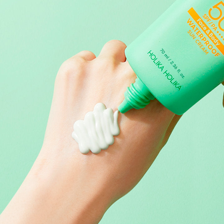Main appliquant HOLIKA HOLIKA Aloe Cica Waterproof Sunscreen 70ml, crème solaire waterproof à l’aloe sur fond vert pastel.