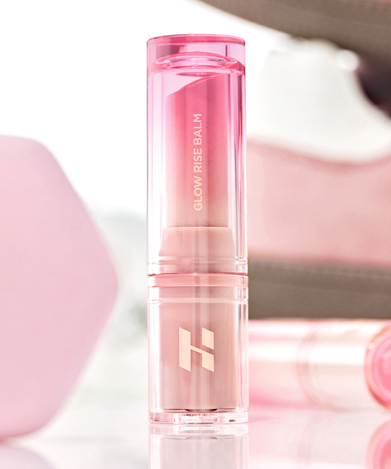 HOLIKA HOLIKA Glow Rise Balm, stick baume rose translucide sur fond doux rose et blanc, gros plan produit de la marque.
