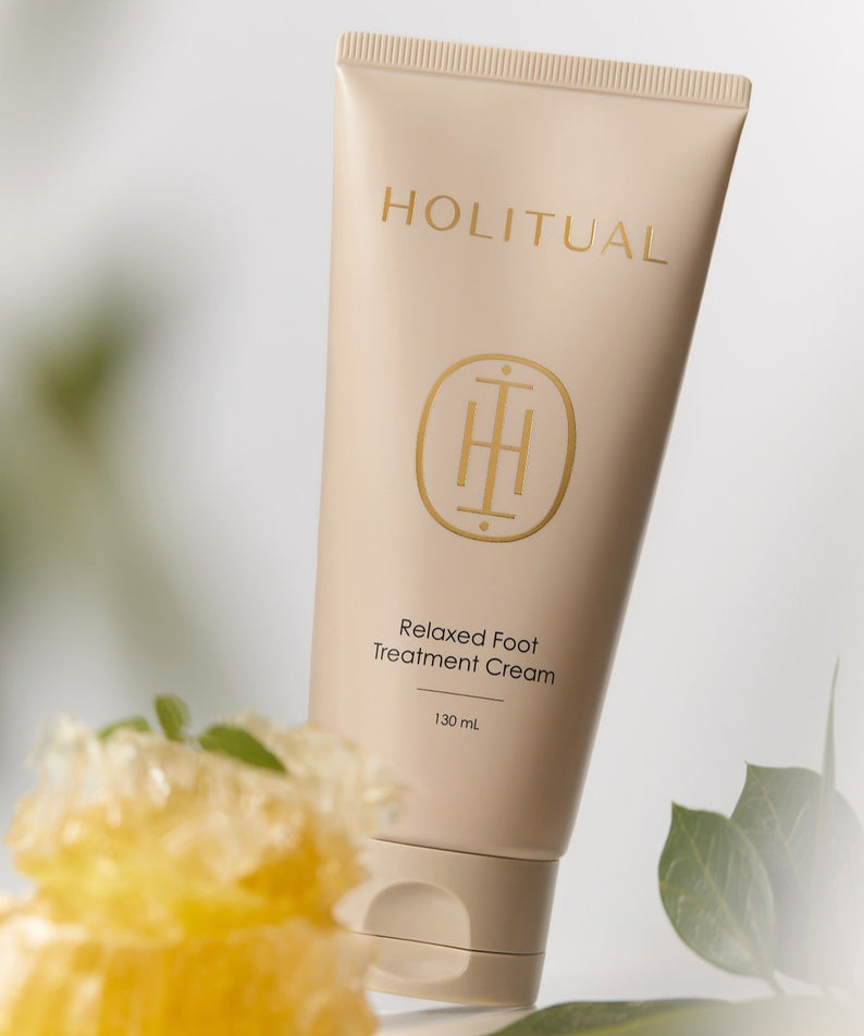 HOLITUAL Relaxed Foot Treatment Cream 130ml, tube beige sur fond clair avec feuilles vertes et fleurs, vue produit.