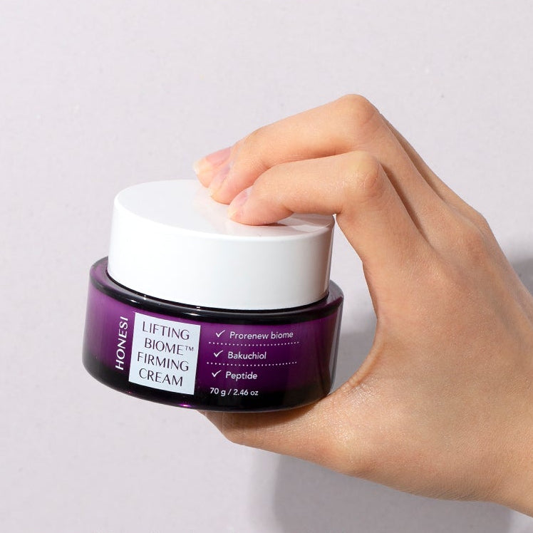 Main tenant le pot HONESI  Lifting Biome Elasticity Cream 70g, crème liftante sur fond clair, branding HONESI visible