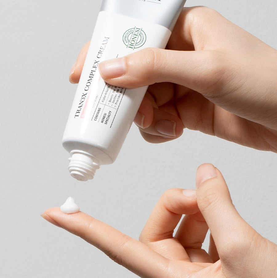 HONESI  Tranex Complex Cream 50ml, main appliquant la crème sur la peau, flacon blanc HONESI sur fond clair.