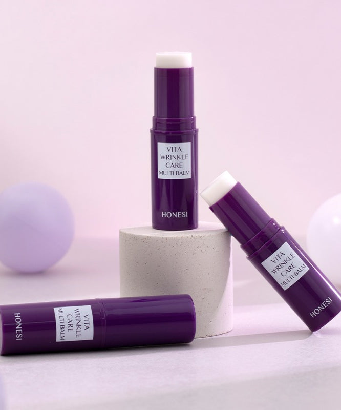 HONESI  Vita Wrinkle Care Multi Balm, baume anti-âge en tube violet, sur fond pastel avec boules décoratives