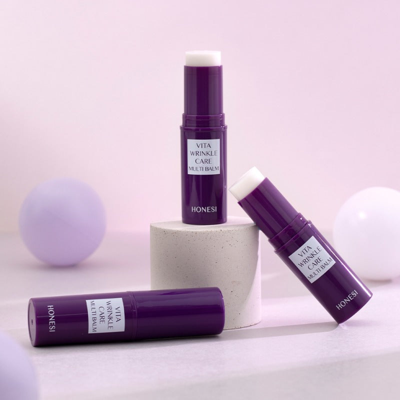 HONESI  Vita Wrinkle Care Multi Balm, baume anti-âge en tube violet, sur fond pastel avec boules décoratives