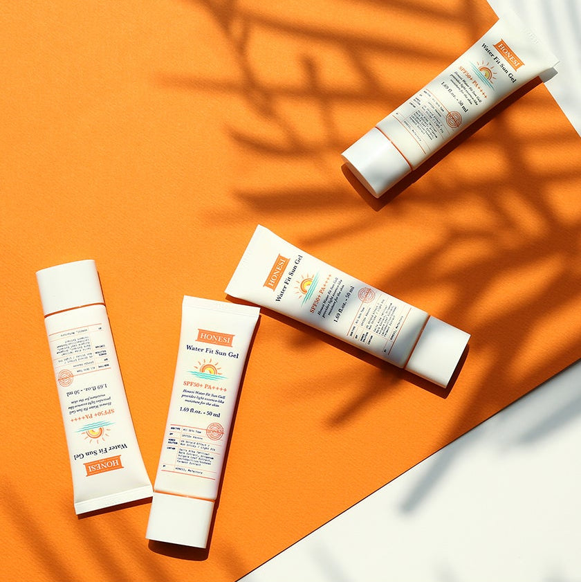HONESI  Water Fit Sun Gel 50ml de la marque HONESI, tubes de crème solaire sur fond orange ensoleillé, ombres