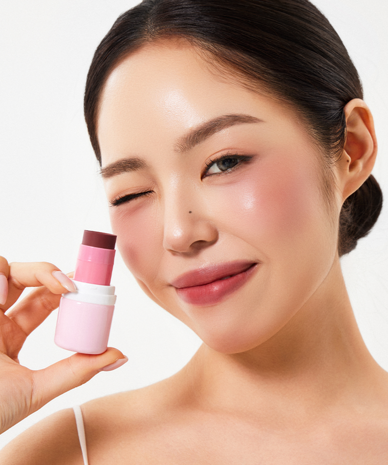 HOUSE OF HUR Every Cheek Blush de la marque, sur peau maquillée : modèle tient le blush rose en studio fond clair.