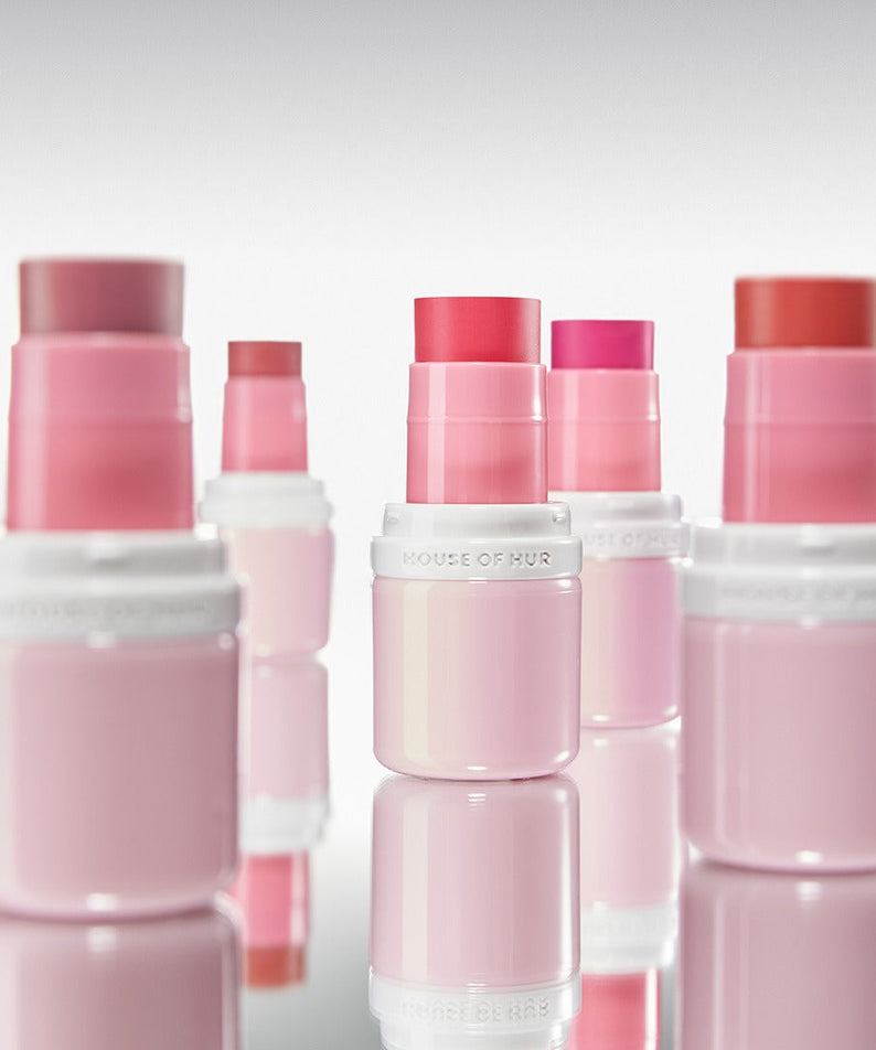 HOUSE OF HUR Every Cheek Blush de la marque, packaging rose sur fond clair, produits cosmétiques en arrière-plan.
