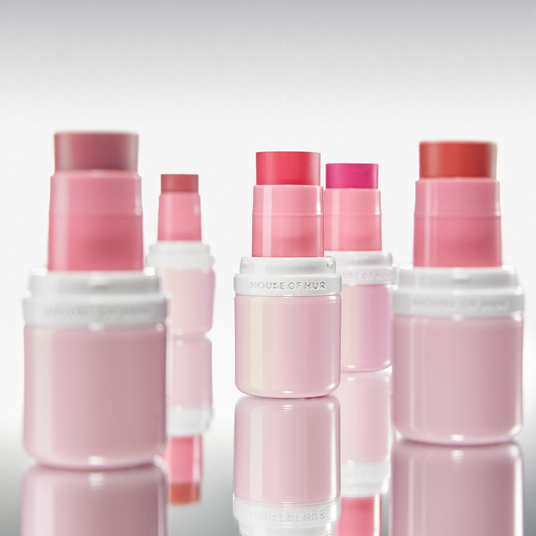 HOUSE OF HUR Every Cheek Blush de la marque, packaging rose sur fond clair, produits cosmétiques en arrière-plan.