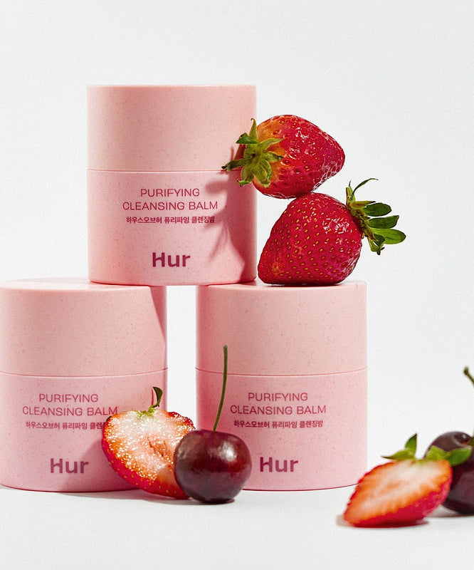 HOUSE OF HUR Purifying Cleansing Balm, baume rose sur fond clair avec fraises et ingrédients, photo produit en studio.