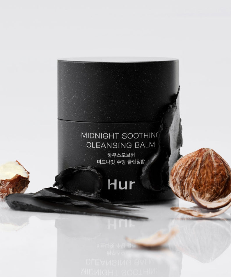 Produit de beauté HOUSE OF HUR Midnight Soothing Cleansing Balm avec emballage élégant en noir, reposant sur une surface réfléchissante.