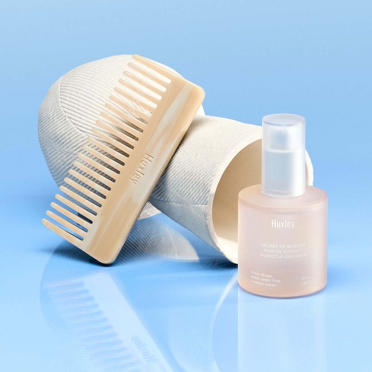 HUXLEY Hair Oil Essence Moroccan Gardener 50ml : flacon Huxley et peigne sur fond bleu, huile capillaire de soins.