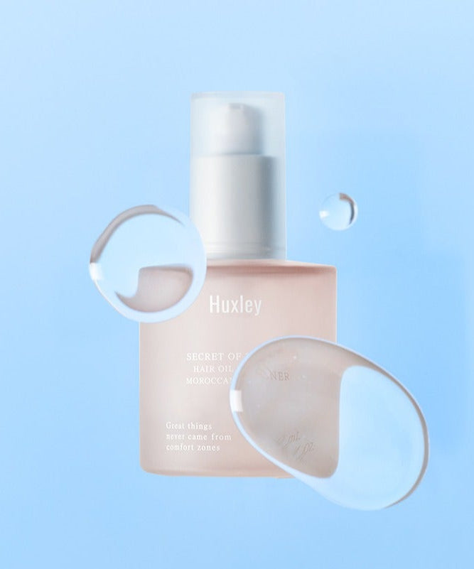 Décris l'image en français : HUXLEY Hair Oil Essence Moroccan Gardener 50ml, flacon Huxley sur fond bleu clair, goutte d'huile.