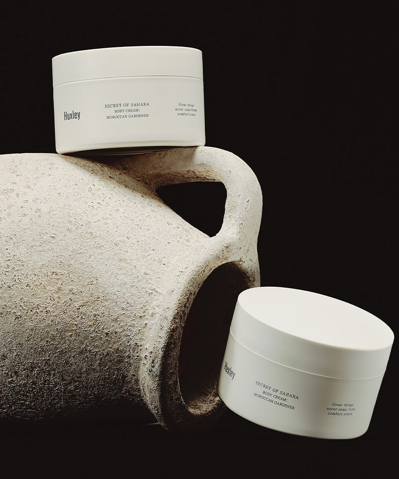 HUXLEY Moroccan Gardener Body Cream 200ml : pot blanc sur galet gris, fond sombre, marque Huxley, contexte spa.