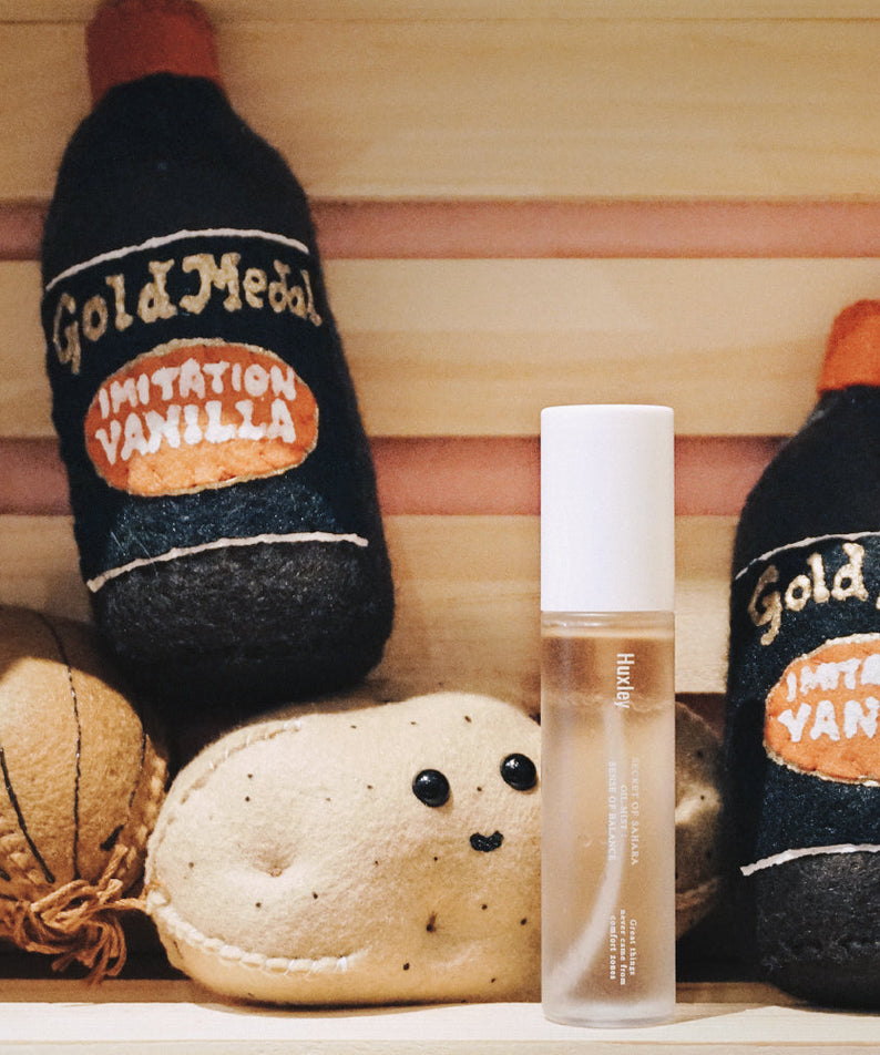 HUXLEY Oil Mist Sense Of Balance entouré de bouteilles décoratives, équilibre et hydratation en un spray élégant.