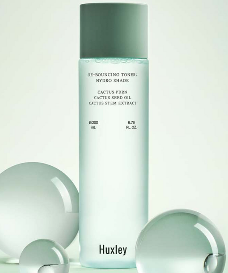 HUXLEY Rebouncing Toner Hydro Shade 200ml, flacon vert sur fond clair avec produits beauté, décor minimaliste.