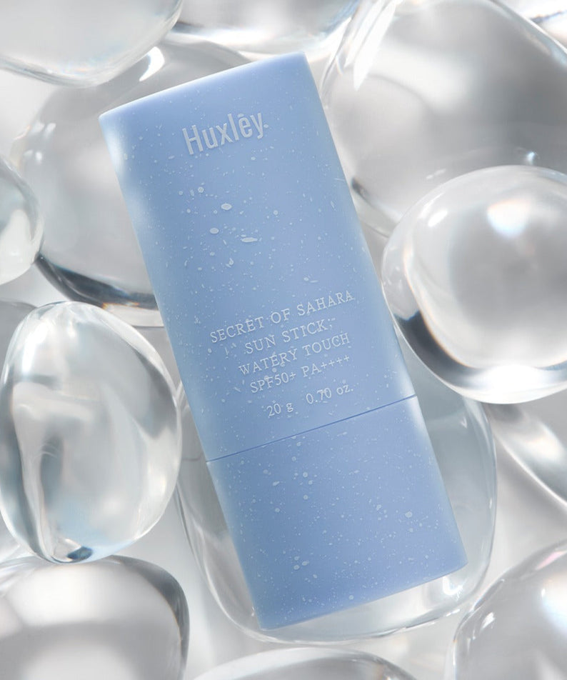 HUXLEY Sun Stick Watery Touch 20g, stick solaire aqueux Huxley sur fond d’éclats de bulles argentées.