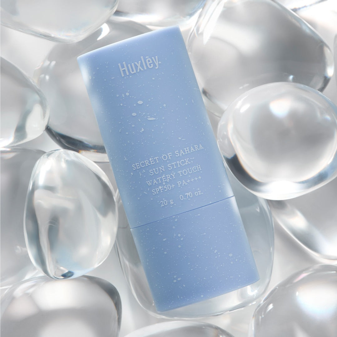 HUXLEY Sun Stick Watery Touch 20g, stick solaire aqueux Huxley sur fond d’éclats de bulles argentées.