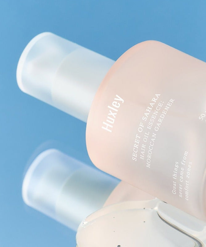 Flacon de HUXLEY Hair Oil Essence Moroccan Gardener 50ml sur fond bleu. Produit de soin capillaire haut de gamme.