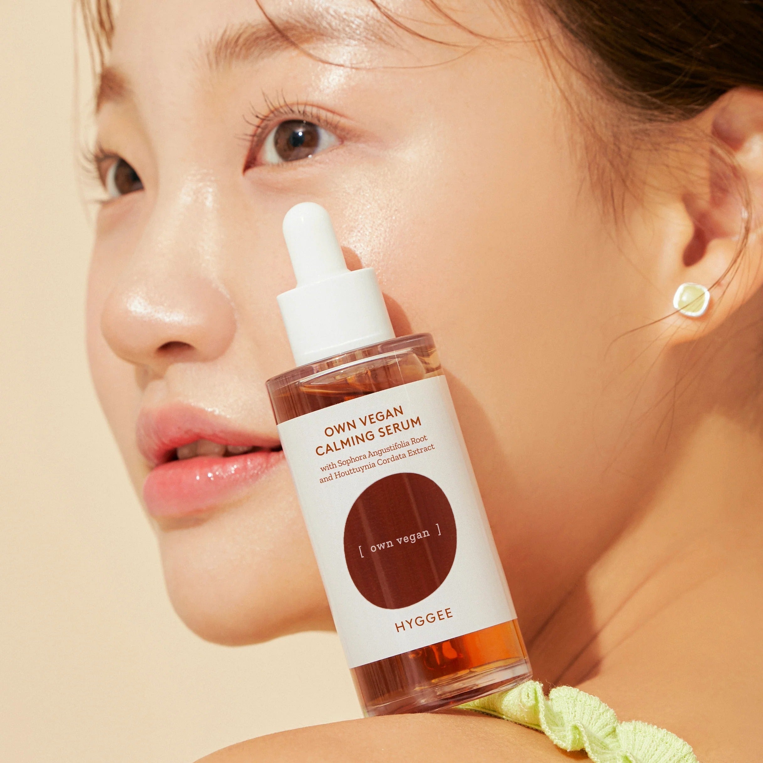 Décris l'image en français : HYGGEE Own Vegan Calming Serum 50ml, sérum apaisant vegan, flacon sur visage, ambiance beauté.