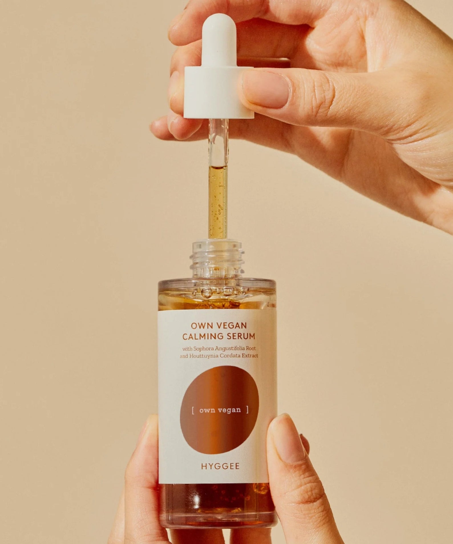 Flacon de HYGGEE Own Vegan Calming Serum 50ml tenu par des mains, avec pipette montrant la texture du sérum apaisant vegan.