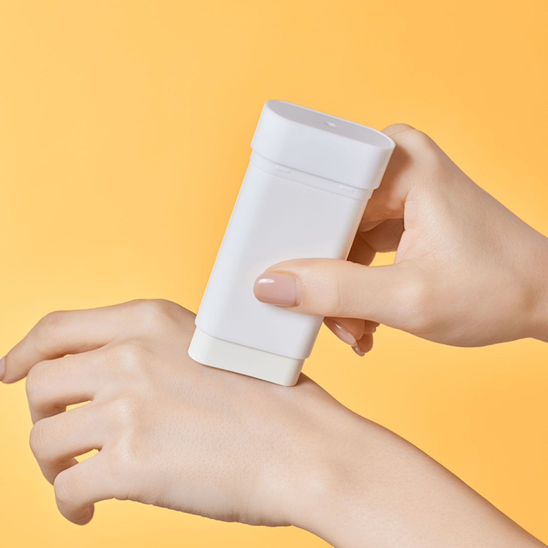 Main tenant ILLIYOON Daily Weaponless Sun Stick 20g, marque sur tube blanc, fond jaune ensoleillé.