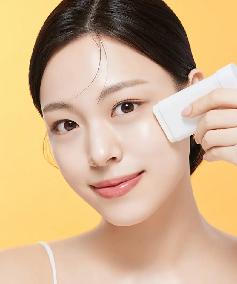 Femme appliquant ILLIYOON Daily Weaponless Sun Stick 20g pour une protection solaire quotidienne en douceur, fond jaune vif.