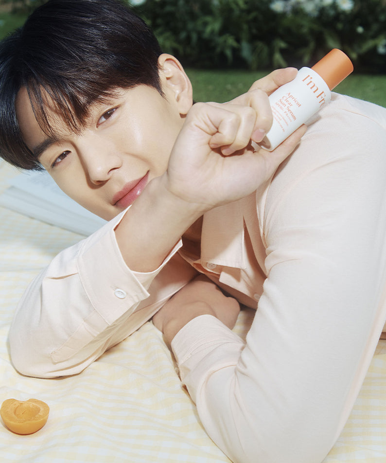 Homme tenant I'M FROM Apricot Clear Sun Serum 50ml, sérum solaire en plein air avec des abricots à côté.