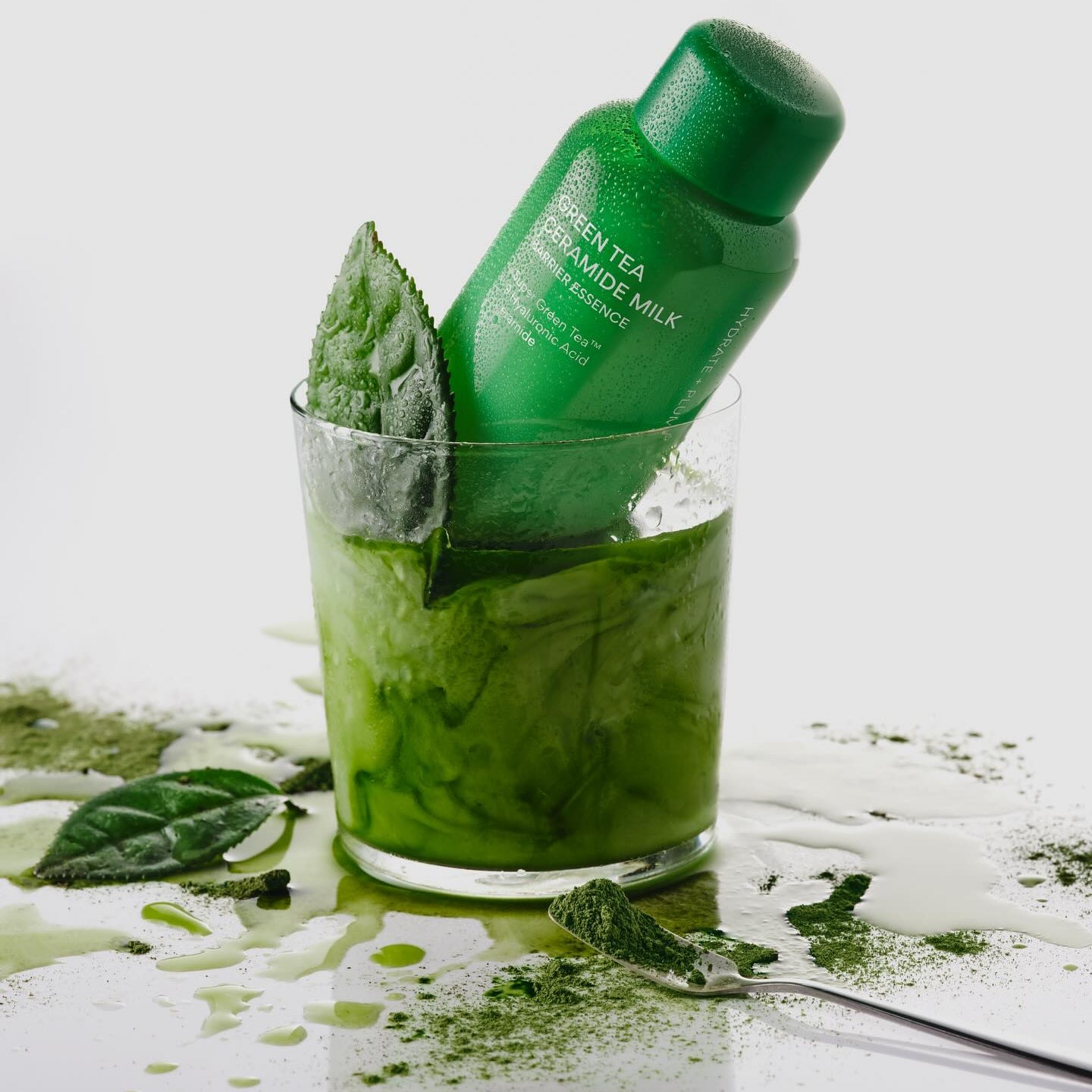 INNISFREE Green Tea Ceramide Milk Essence 160ml en flacon vert, entouré de feuilles de thé vert et splash, sur fond blanc